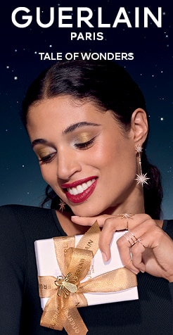 Guerlain luxus ajándékdoboz arany masnival, elegáns csillagos háttérrel.